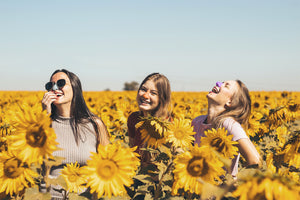 Three girls laughing in sunflower field wearing colorful and best spf for face. 